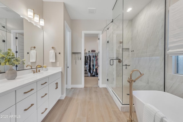 bathroom featuring wood finished floors, vanity, a freestanding bath, a stall shower, and a walk in closet