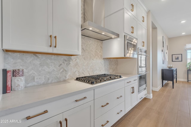 kitchen with white cabinets, wall chimney exhaust hood, light stone counters, stainless steel appliances, and backsplash