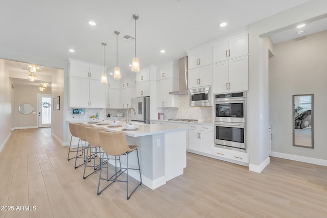 kitchen featuring a kitchen breakfast bar, light countertops, appliances with stainless steel finishes, wall chimney exhaust hood, and tasteful backsplash