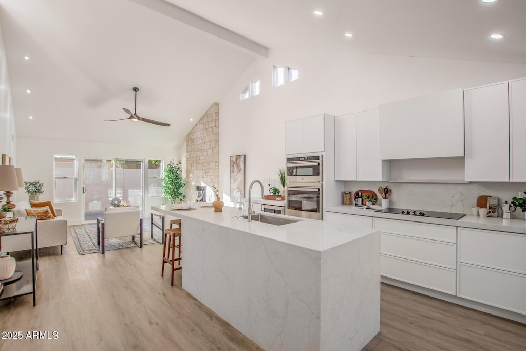 kitchen with sink, white cabinetry, light hardwood / wood-style floors, a center island with sink, and black electric cooktop