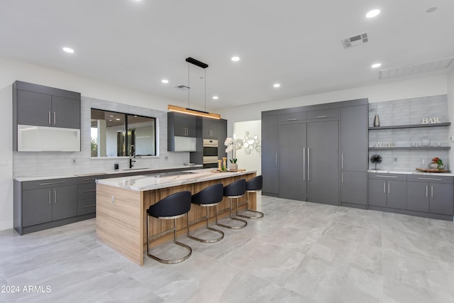 kitchen with backsplash, a breakfast bar, gray cabinets, a kitchen island, and hanging light fixtures