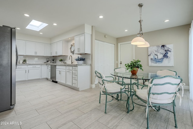 kitchen with a skylight, tasteful backsplash, stainless steel appliances, white cabinetry, and hanging light fixtures