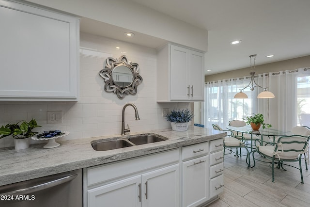 kitchen with light stone countertops, sink, hanging light fixtures, stainless steel dishwasher, and white cabinets