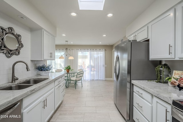 kitchen with white cabinets, decorative backsplash, sink, and a skylight