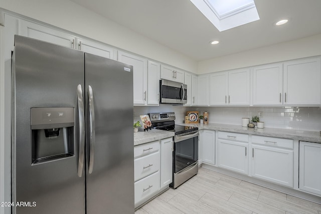 kitchen featuring white cabinets, appliances with stainless steel finishes, a skylight, and light stone countertops