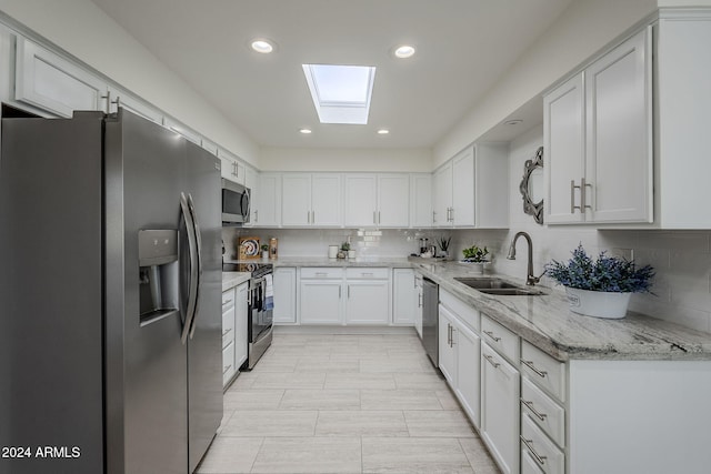 kitchen with appliances with stainless steel finishes, a skylight, tasteful backsplash, sink, and white cabinets