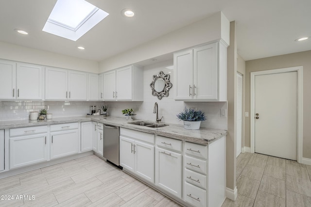 kitchen with a skylight, sink, stainless steel dishwasher, backsplash, and white cabinets