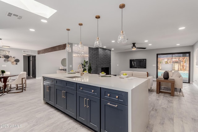 kitchen featuring sink, light hardwood / wood-style floors, an island with sink, and hanging light fixtures