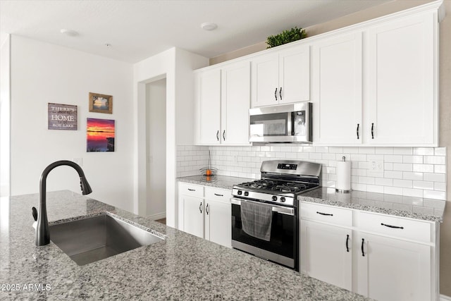 kitchen featuring sink, white cabinetry, light stone counters, appliances with stainless steel finishes, and decorative backsplash