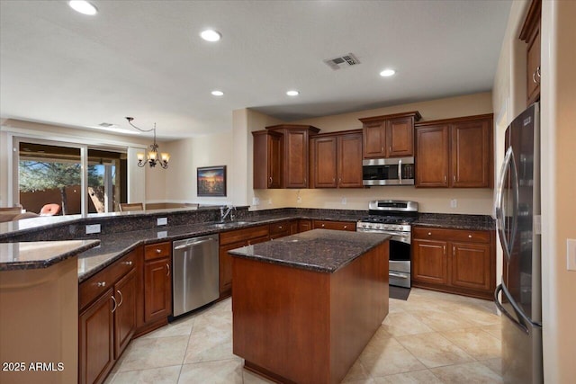 kitchen with a center island, stainless steel appliances, dark stone counters, sink, and hanging light fixtures