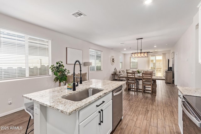 kitchen featuring wood finished floors, stainless steel appliances, a sink, white cabinetry, and visible vents