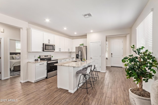 kitchen with appliances with stainless steel finishes, visible vents, tasteful backsplash, and white cabinetry