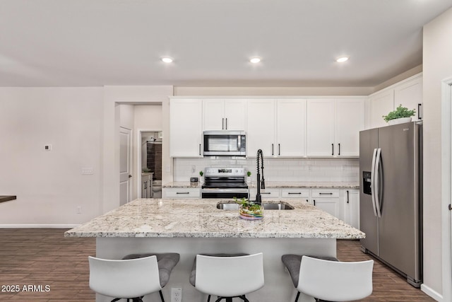 kitchen with dark wood-style floors, a sink, stainless steel appliances, a breakfast bar area, and backsplash