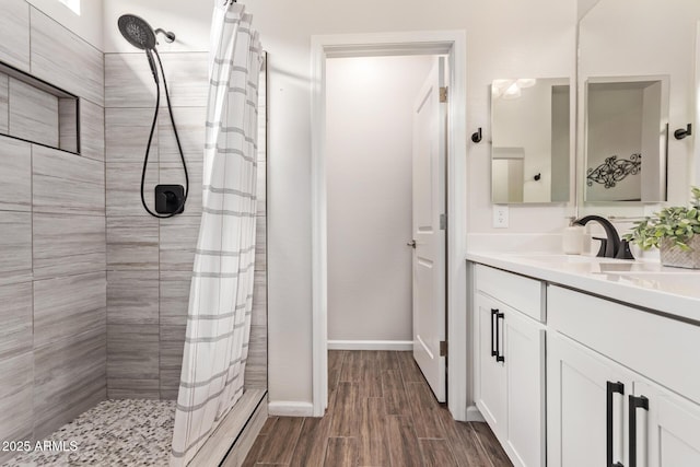 bathroom with baseboards, tiled shower, wood finished floors, and vanity