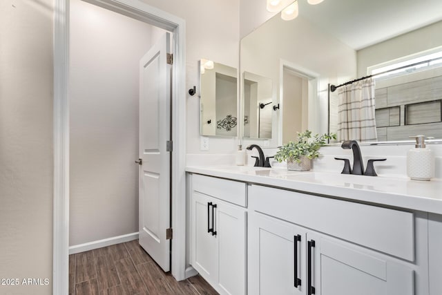 full bath with double vanity, wood finished floors, baseboards, and a sink
