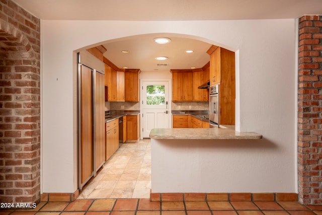 kitchen with tasteful backsplash, paneled built in refrigerator, kitchen peninsula, black dishwasher, and stainless steel oven