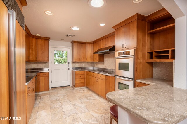 kitchen with a breakfast bar, stovetop, kitchen peninsula, double wall oven, and backsplash