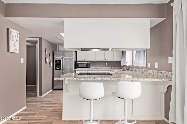 kitchen featuring appliances with stainless steel finishes, kitchen peninsula, a breakfast bar area, and white cabinets