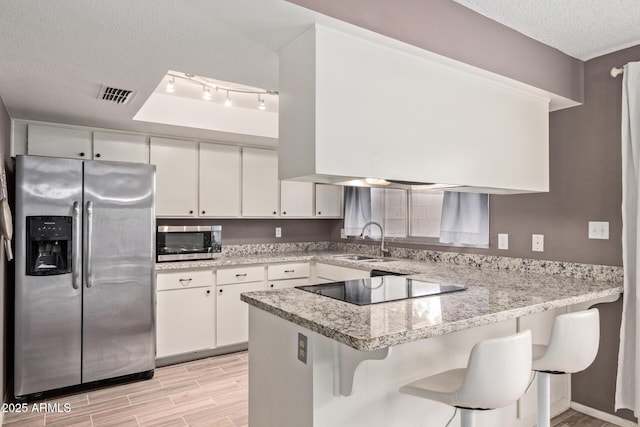 kitchen featuring appliances with stainless steel finishes, white cabinetry, sink, a kitchen breakfast bar, and kitchen peninsula