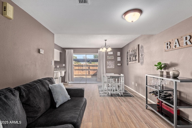 living room featuring a notable chandelier, light hardwood / wood-style flooring, and a textured ceiling