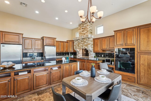 kitchen with decorative backsplash, a towering ceiling, a notable chandelier, stainless steel refrigerator, and hanging light fixtures