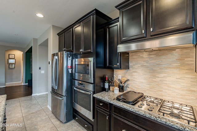 kitchen featuring light stone countertops, stainless steel appliances, light tile patterned floors, and tasteful backsplash