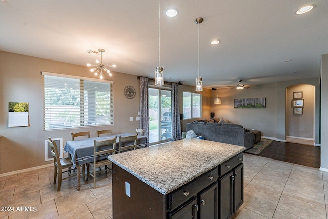 kitchen with ceiling fan with notable chandelier, decorative light fixtures, light stone countertops, and a kitchen island