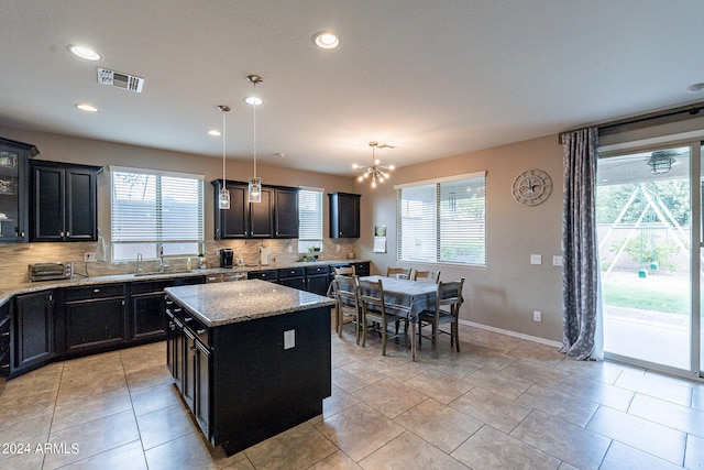 kitchen with pendant lighting, a center island, a notable chandelier, decorative backsplash, and light stone countertops