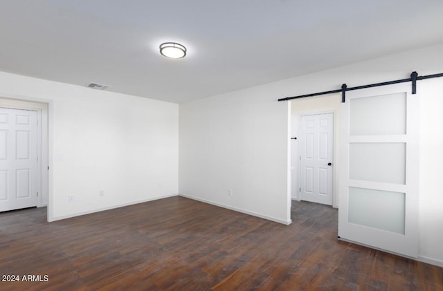 spare room with a barn door and dark wood-type flooring