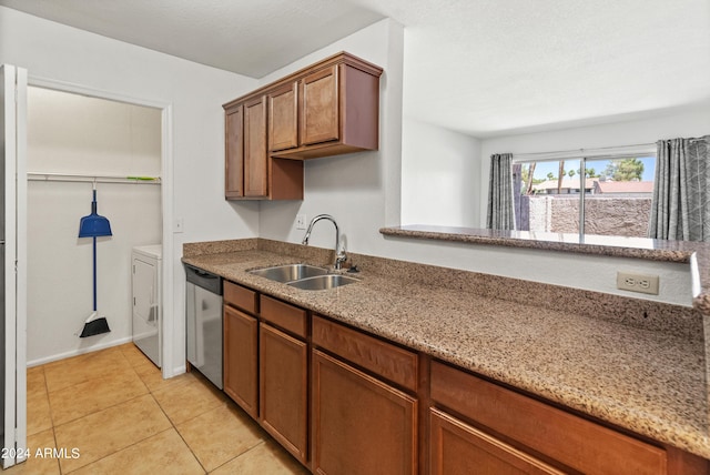 kitchen featuring light stone counters, stainless steel dishwasher, sink, washer / clothes dryer, and light tile patterned flooring