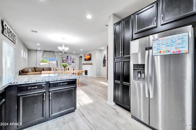 kitchen with an inviting chandelier, light wood-type flooring, light stone counters, and stainless steel refrigerator with ice dispenser