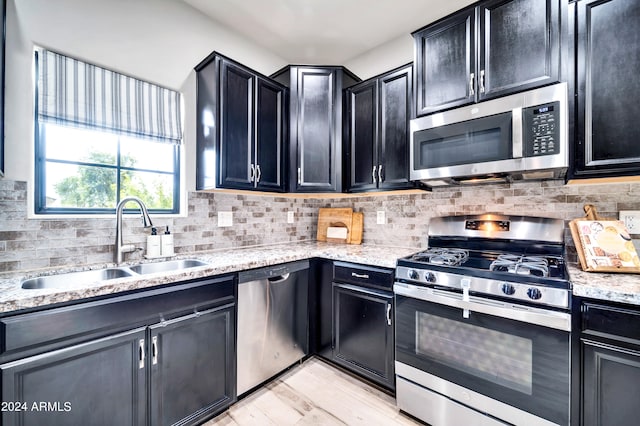 kitchen featuring appliances with stainless steel finishes, light stone countertops, sink, tasteful backsplash, and light hardwood / wood-style flooring