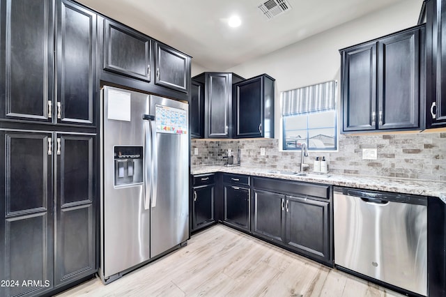 kitchen featuring stainless steel appliances, light wood-type flooring, sink, tasteful backsplash, and light stone counters