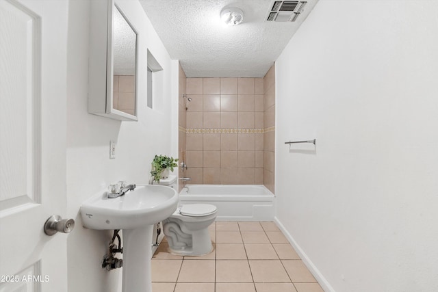 bathroom featuring tiled shower / bath, tile patterned floors, toilet, and a textured ceiling