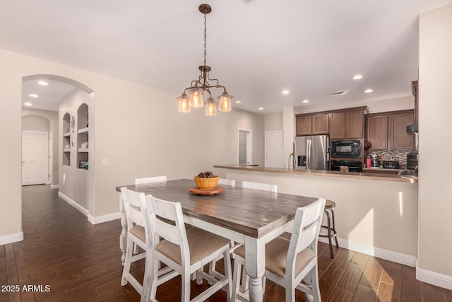 dining area with built in shelves, dark hardwood / wood-style flooring, and an inviting chandelier