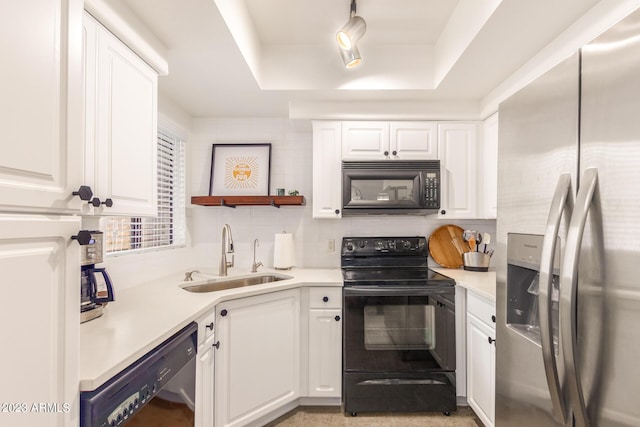 kitchen with a tray ceiling, light countertops, white cabinets, a sink, and black appliances