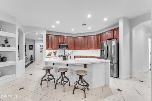 kitchen featuring an island with sink, a kitchen breakfast bar, light tile patterned floors, stainless steel appliances, and built in shelves