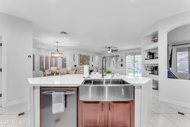 kitchen with sink, light tile patterned floors, hanging light fixtures, an island with sink, and stainless steel dishwasher