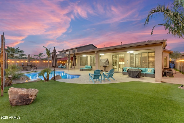 pool at dusk with an outdoor living space, a lawn, and a patio area