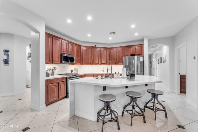 kitchen with appliances with stainless steel finishes, a kitchen island with sink, a breakfast bar area, and light tile patterned floors