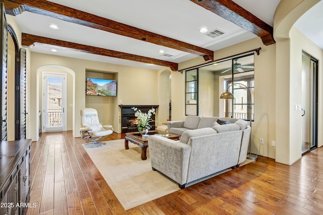 living room with arched walkways, beamed ceiling, hardwood / wood-style flooring, a ceiling fan, and recessed lighting