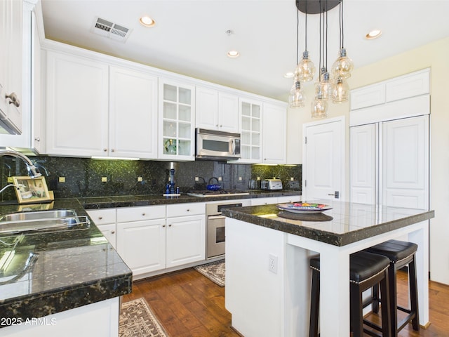 kitchen with appliances with stainless steel finishes, a kitchen bar, white cabinets, dark wood-style flooring, and dark countertops