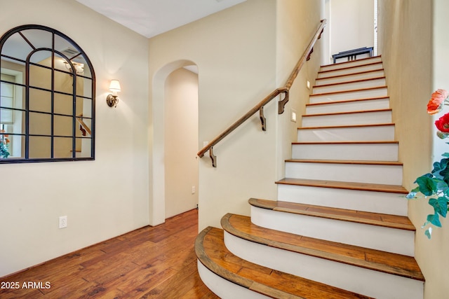 staircase with arched walkways and wood-type flooring