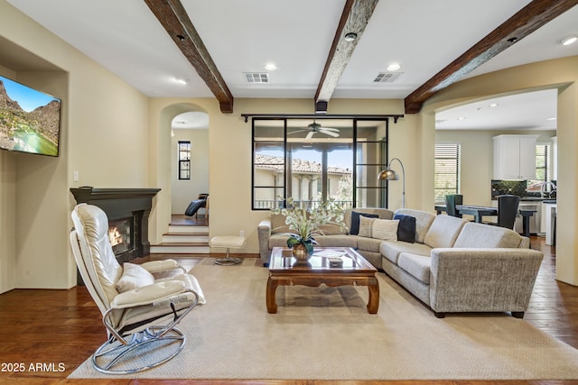 living room featuring dark wood-type flooring, arched walkways, recessed lighting, beam ceiling, and ceiling fan