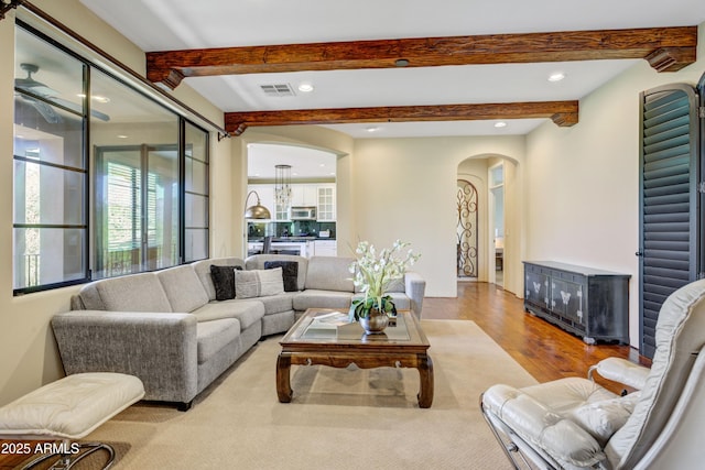 living room featuring arched walkways, wood finished floors, beamed ceiling, and recessed lighting