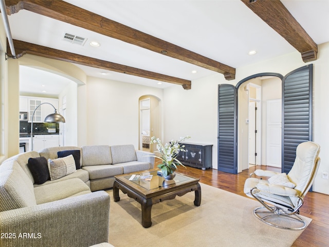 living room with arched walkways, wood finished floors, beamed ceiling, and recessed lighting