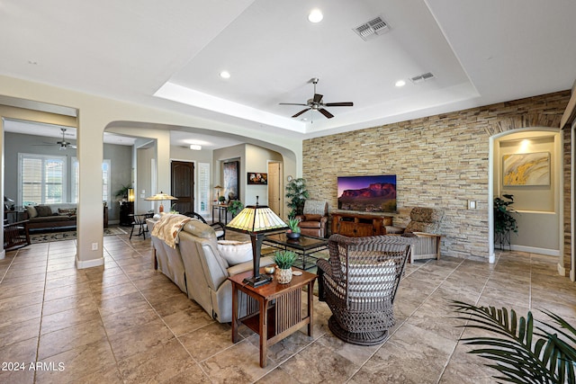 living room featuring a raised ceiling, ceiling fan, and light tile flooring