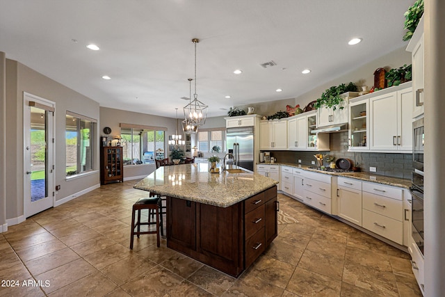 kitchen with an island with sink, tile floors, built in appliances, backsplash, and pendant lighting