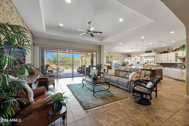 living room featuring ceiling fan, a tray ceiling, and light tile flooring