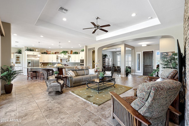 living room with a tray ceiling, light tile flooring, and ceiling fan